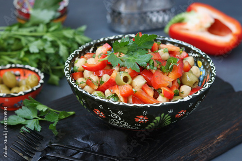 Healthy salad of chickpea  green olives  pepper and parsley located on wooden board on a dark background  Horizontal format