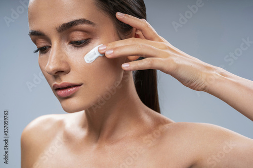 Young woman putting moisture cream on cheeck photo