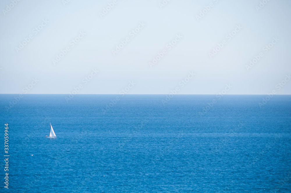 Lone white sailboat on a stretch of a bright blue sea. Sunny day. Mediterranean sea.