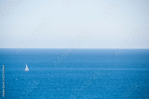 Lone white sailboat on a stretch of a bright blue sea. Sunny day. Mediterranean sea.