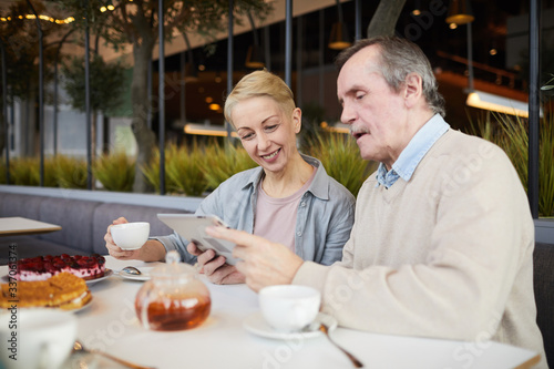 Smiling mature couple watching something on digital tablet while drinking tea in the restaurant