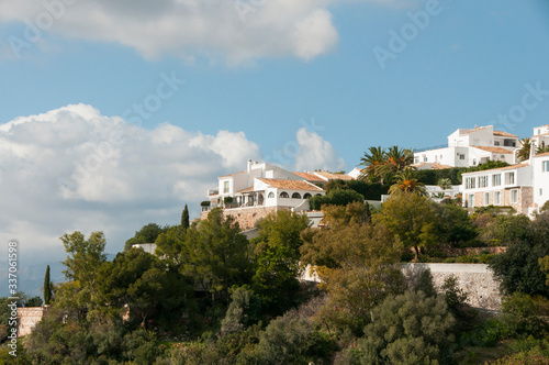 White spanish village on a green hill. White spanish houses surrounded by greenery against a blue sky. Mediterranean architecture. © asyashu