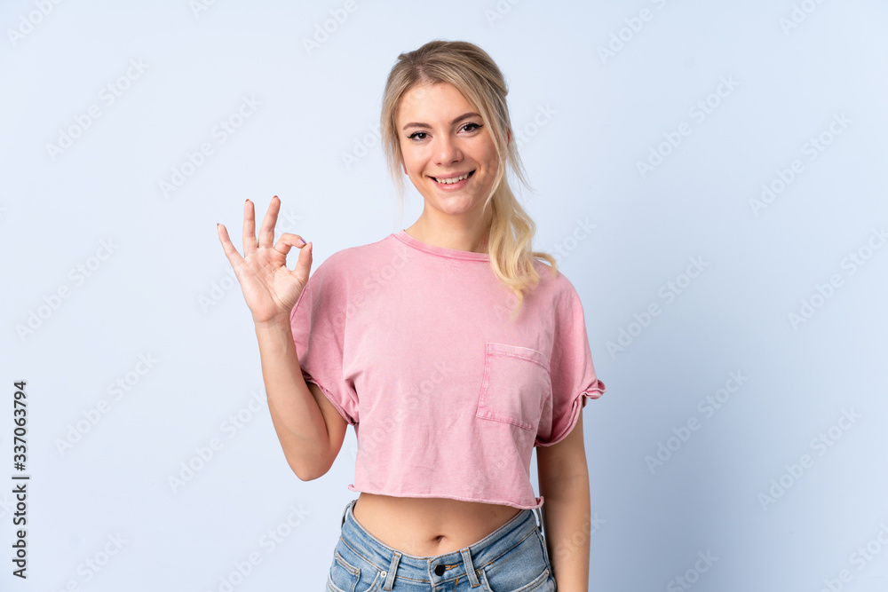 Blonde woman over isolated blue background showing ok sign with fingers Blonde woman over isolated blue background showing ok sign with fingers