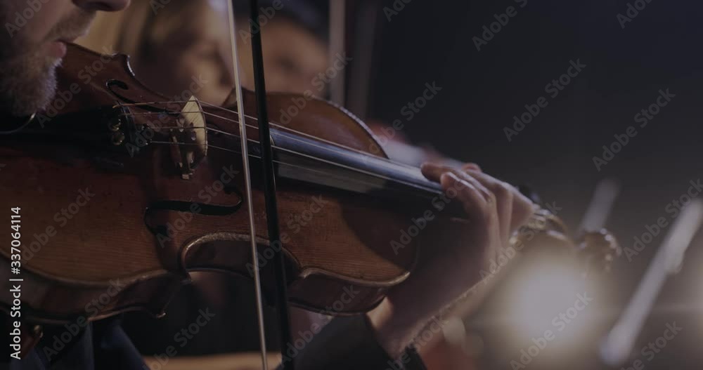 Close up of violin in hands of Caucasian man while he performing in classical orchestra. Male violinist playing on instrument at concert. Virtuoso concept. Classic band performance.
