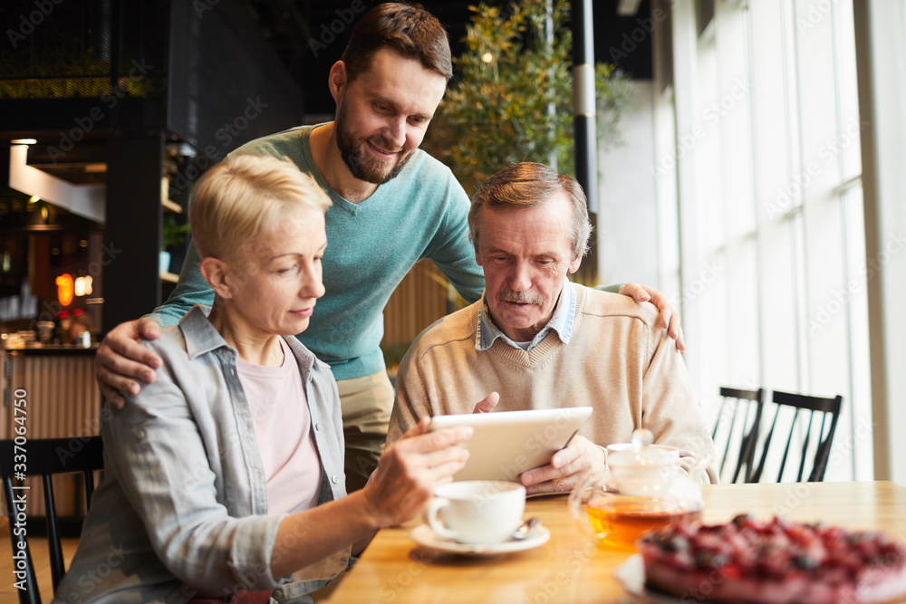Mature parents and their son using digital tablet for online conversation while drinking tea in the restaurant Mature parents and their son using digital tablet for online conversation while drinking tea in the restaurant