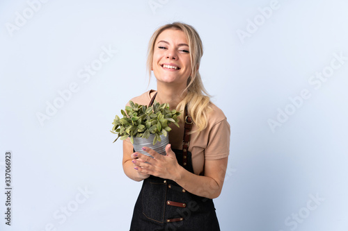 Blonde gardener woman holding a plant over isolated background applauding