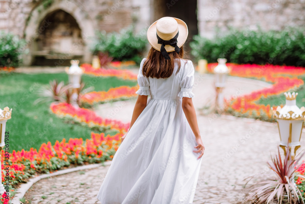 girl in a white dress and a straw hat walks in a beautiful park. bride in a vintage wedding dress in the garden.