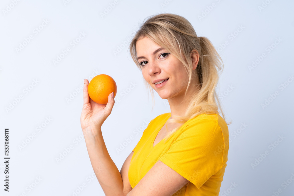 Blonde woman over isolated blue background holding an orange Blonde woman over isolated blue background holding an orange