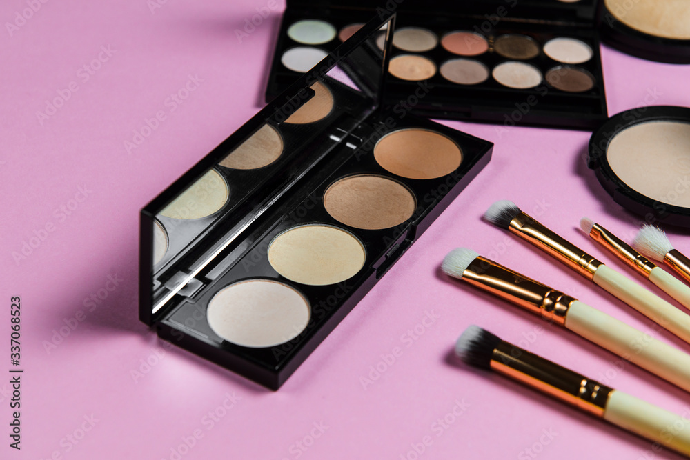 Makeup brushes, powder, eyeshadow palette, foundation for the face on a light pink background with place for text, side view Makeup brushes, powder, eyeshadow palette, foundation for the face on a light pink background with place for text, side view