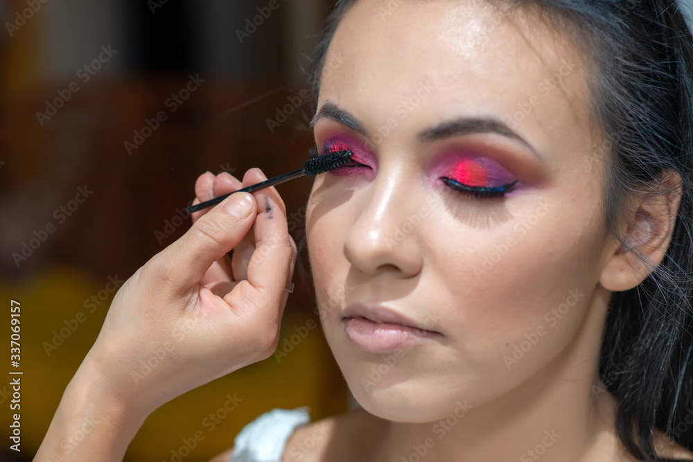 Woman applying black mascara on eyelashes with makeup brush. Make up artist doing professional make up of beautiful young woman. 