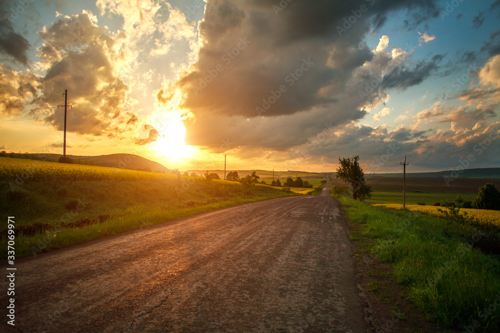 Empty asphalt road among country green yellow fields at sunset sky