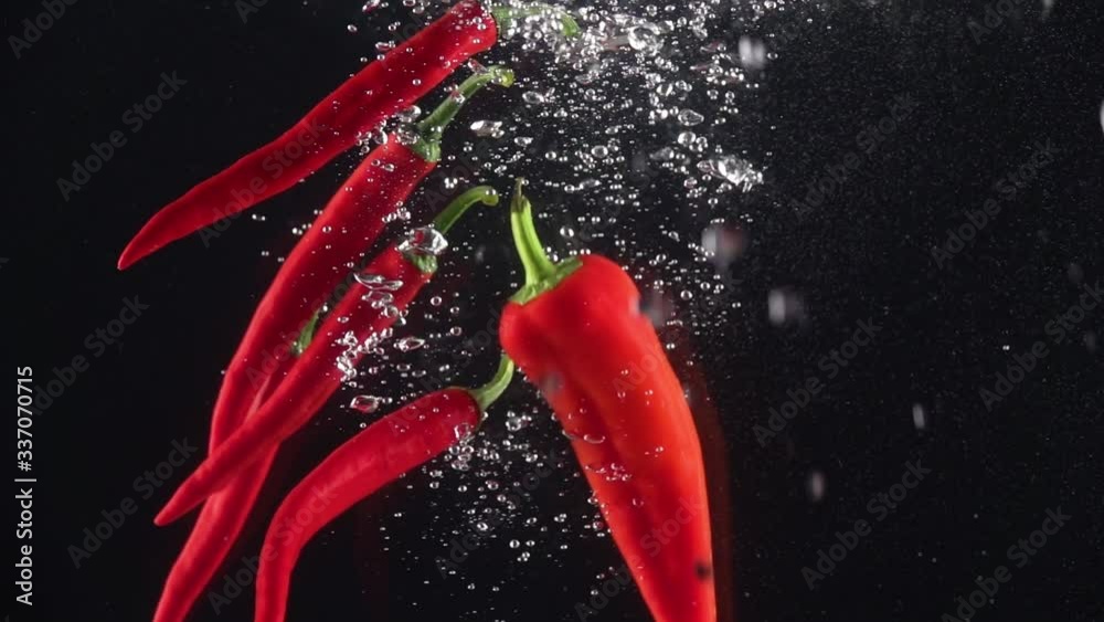 Hot red chilli peppers falling into the water on a black background. Slow motion