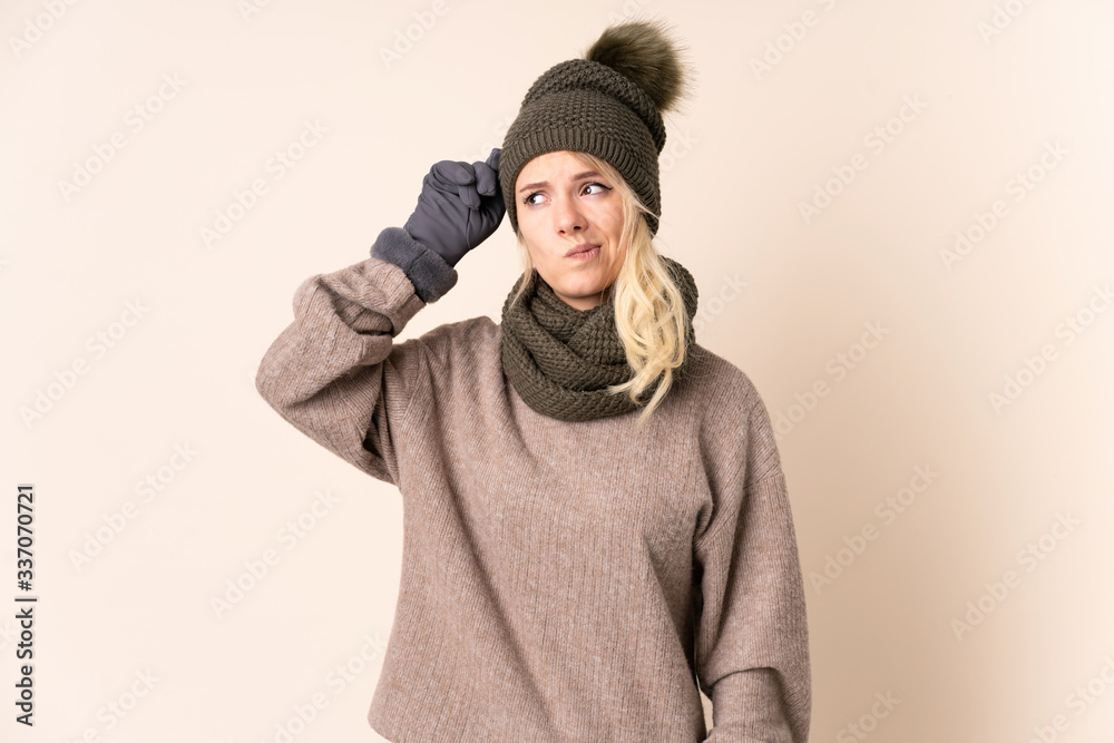 Young woman with winter hat over isolated background having doubts and with confuse face expression Young woman with winter hat over isolated background having doubts and with confuse face expression