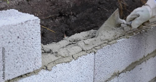 bricklayer building wall from ceramsite concrete blocks, applying mortar with trowel photo