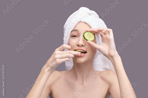 Young girl holding cucumber slice in hand. Nature mask concept. Face skincare routine. Lifting effect. Happy woman portrait. Dermatology homemade healthcare procedure. Copyspace. Hiding eye