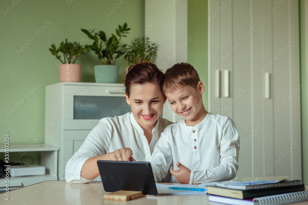 distance learning, online education at home during the covid-19 pandemic. family mom and son joyfully doing homework in the room using tablet distance learning, online education at home during the covid-19 pandemic. family mom and son joyfully doing homework in the room using tablet