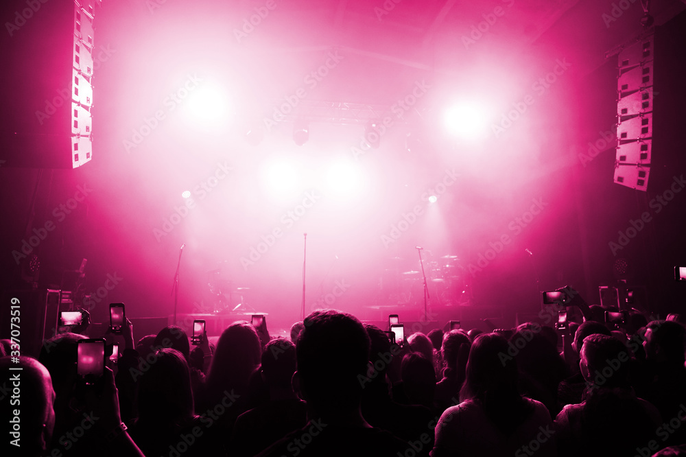 the crowd at a concert festival takes photos and videos on a smartphone. banner for a music show. people's backs you are pink lit in front of the stage