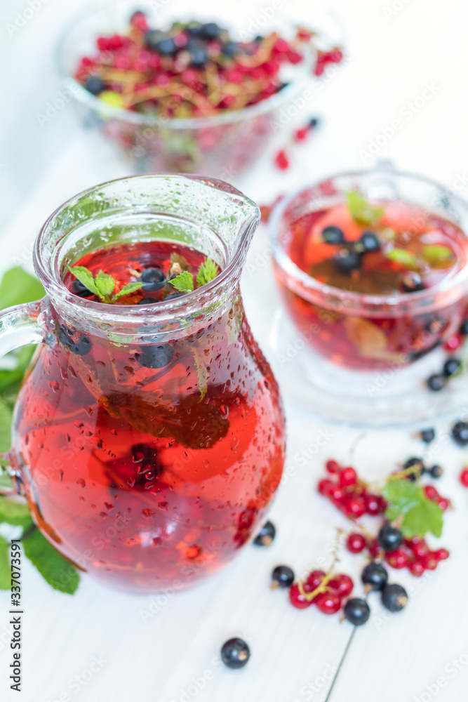 Red and black currant fruit drink in transparent glass cup. Clear glass vase with red and black currant berries on the white wooden background Red and black currant fruit drink in transparent glass cup. Clear glass vase with red and black currant berries on the white wooden background