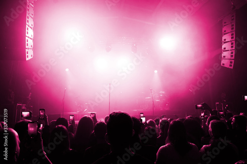 the crowd at a concert festival takes photos and videos on a smartphone. banner for a music show. people's backs you are pink lit in front of the stage