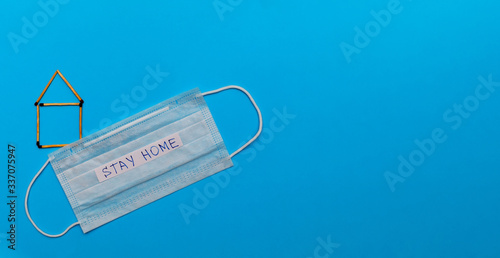 A house of matches and a medical face mask with the text stay home on a blue background. Medical concept. Self-isolation, quarantine, pandemic, coronavirus. Flat lay, copy space, top view.