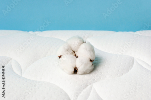 Cotton flowers on a comfortable mattress texture background top view. White texture of mattress bedding background. Healthy sleep concept, comfortable bed. Tender air background with cotton © olgaarkhipenko