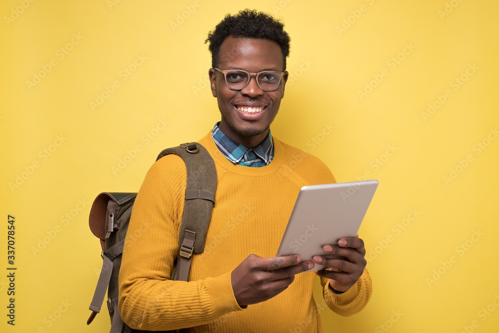 Happy african american college student in glasses holding tablet on yellow wall. Studio shot Happy african american college student in glasses holding tablet on yellow wall. Studio shot