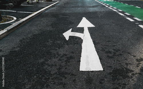 Road marking on the asphalt: white paint branch arrow pointing forward and to the left, a fragment of a green bicycle lane on the right after the division line, Europe, Portugal, Lisbon