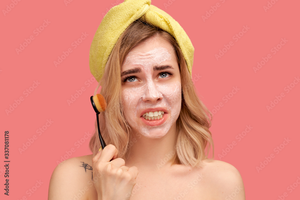 Unhappy young girl holds brush to clean face, has dissatisfied expression , asks God what this punishment is for.. Beautiful woman with yellow hat or towel stands naked against pink wall Studio Unhappy young girl holds brush to clean face, has dissatisfied expression , asks God what this punishment is for.. Beautiful woman with yellow hat or towel stands naked against pink wall Studio