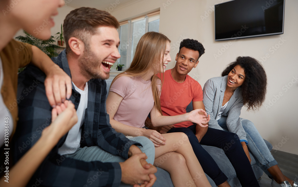 Having fun at home. Group of young happy multicultural people in casual wear enjoying time together while sitting on the sofa in the modern apartment. Friendship Having fun at home. Group of young happy multicultural people in casual wear enjoying time together while sitting on the sofa in the modern apartment. Friendship