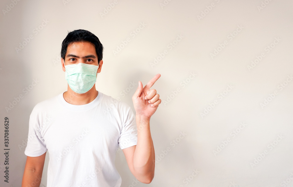 Portrait of handsome young Asian man wearing a medical protective mask pointing his finger at side copy space. Concept of fighting against coronavirus covid-19. Confident male model isolated on white Portrait of handsome young Asian man wearing a medical protective mask pointing his finger at side copy space. Concept of fighting against coronavirus covid-19. Confident male model isolated on white