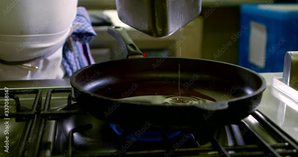 Close-up of the hands of the cook, who is in the kitchen pouring oil into a pan that is on the stove with a ladle, on his hands he is wearing blue gloves. Close-up of the hands of the cook, who is in the kitchen pouring oil into a pan that is on the stove with a ladle, on his hands he is wearing blue gloves.