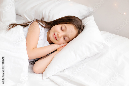 Little brunette girl sleeps sweetly in bed with white linen. space for text. healthy baby's sleep