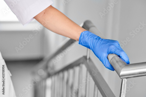 A hand in a blue glove holds a handrail in a hospital