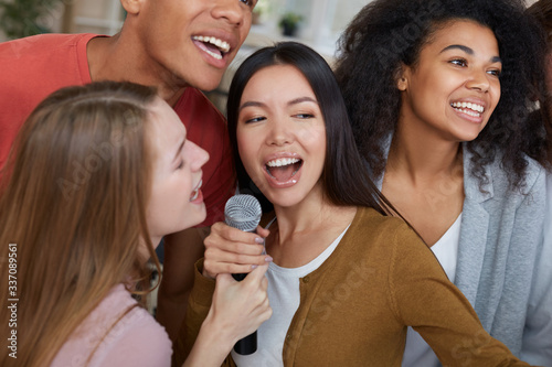 Karaoke party. Group of young and happy multicultural friends in casual wear singing with microphone together while playing karaoke at home. Friendship. Home entertainment