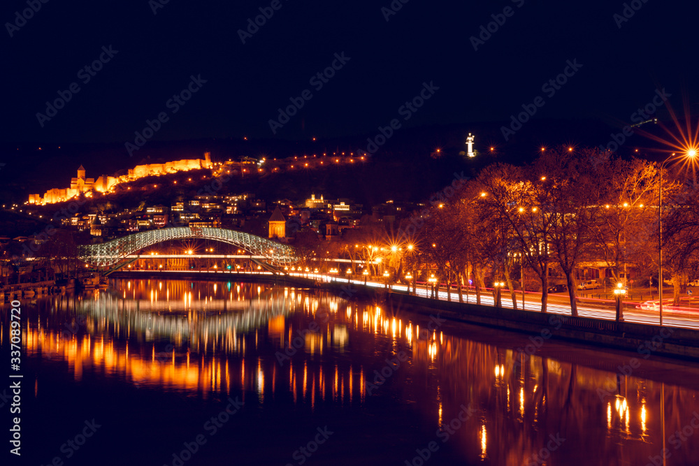 Romatic Panoramic night view to the bridge of peace and its reflections, and old town with car trails. Travel destination and night photography in Tbilisi.georgia.2020