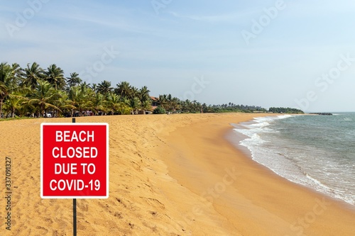 ''Beach closed due to COVID-19'' information sign against a desolate tropical beach
