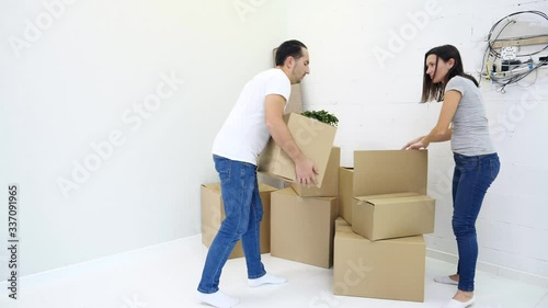 Tired guy is bringing heavy boxes in room suffering from backache touching back with unhappy face during relocation. photo