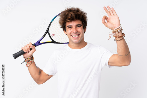 Young caucasian man over isolated white background playing tennis and making OK sign