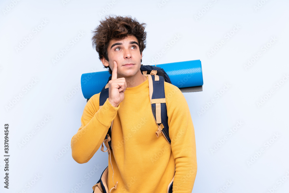 Young mountaineer man with a big backpack over isolated blue background thinking an idea Young mountaineer man with a big backpack over isolated blue background thinking an idea