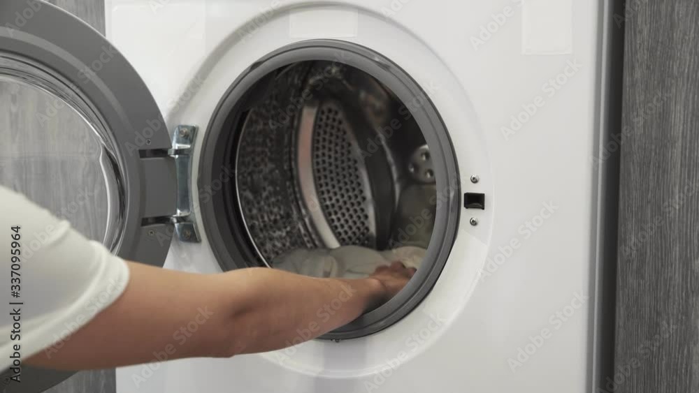 Female hand with married ring takes WHITE CLOTHES from laundry machine. Loading washing machine. Load clothes to washer machine. Load clothes laundry washing machine. Preparing laundry washing