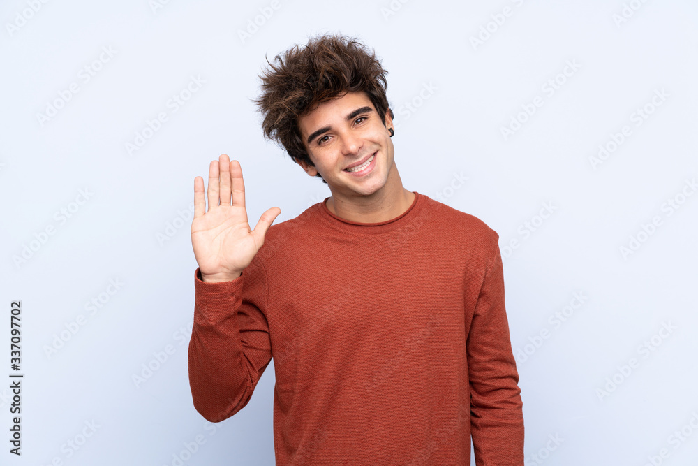 Young caucasian man over isolated blue background saluting with hand with happy expression Young caucasian man over isolated blue background saluting with hand with happy expression