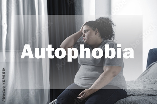 Depressed overweight woman sitting alone on bed at home. Autophobia photo