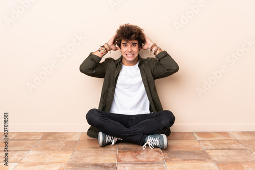 Young caucasian man sitting on the floor frustrated and takes hands on head