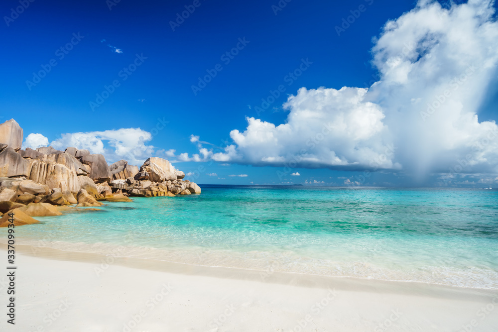 Bright sunny day at grand Anse beach at La Digue island in Seychelles. Sandy beach with blue ocean bay, white clouds in background