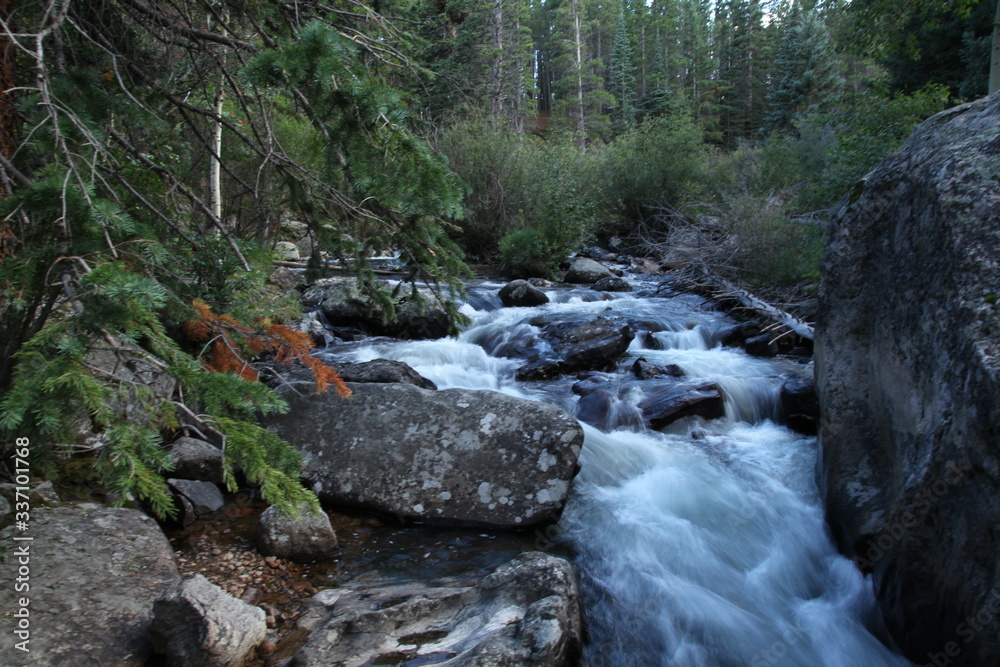Rocky Mountain waterfalls and streams with smooth flowing water over boulders in pine trees Rocky Mountain waterfalls and streams with smooth flowing water over boulders in pine trees