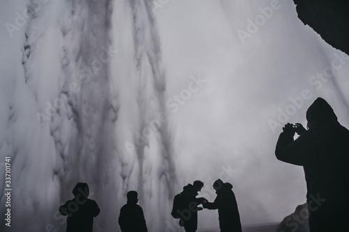 Inspiring travel landscape, beautiful Seljalandsfoss waterfall in Iceland, persons standing behind the stream, famous Icelandic landmark