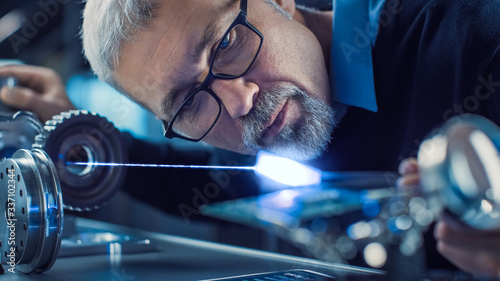Εκτύπωση καμβά Close-up Portrait of Focused Middle Aged Engineer in Glasses Working with High Precision Laser Equipment, Using Lenses and Optics for Accuracy Electronics