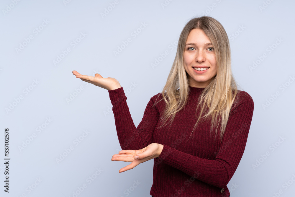 Young blonde woman over isolated blue background extending hands to the side for inviting to come Young blonde woman over isolated blue background extending hands to the side for inviting to come