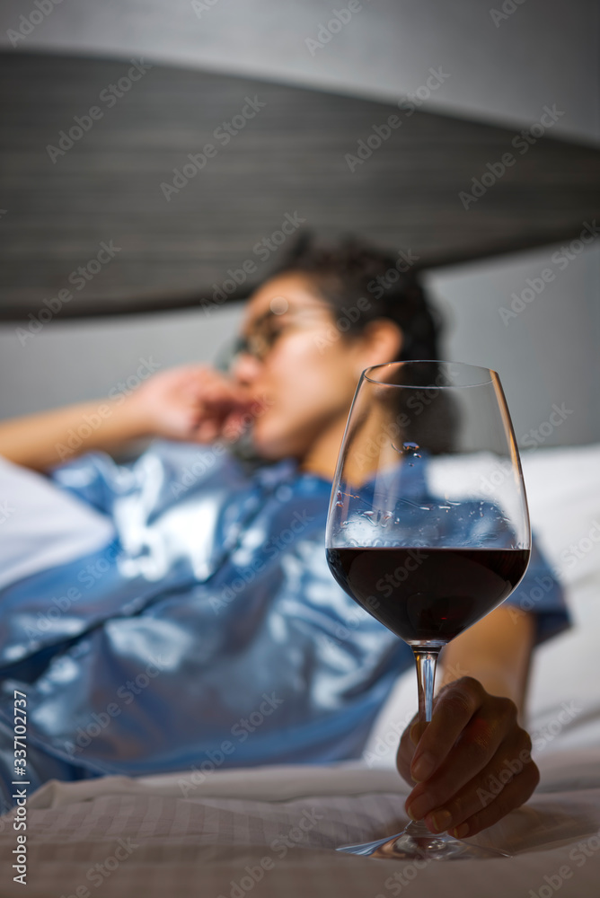 A distraught woman wearing satin pajamas sits in bed with a glass of wine A distraught woman wearing satin pajamas sits in bed with a glass of wine