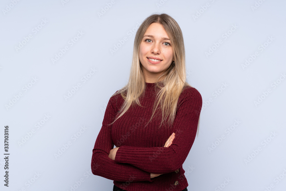 Young blonde woman over isolated blue background with arms crossed and looking forward Young blonde woman over isolated blue background with arms crossed and looking forward